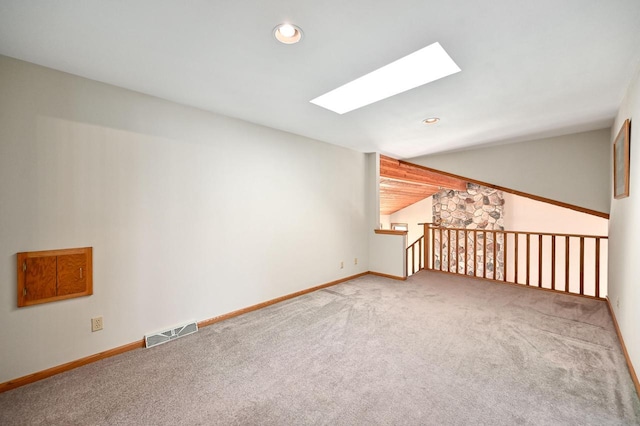 spare room with visible vents, vaulted ceiling with skylight, carpet, and baseboards