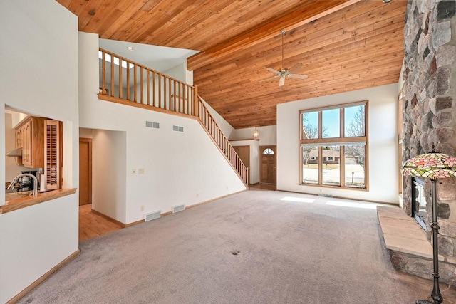 unfurnished living room featuring visible vents, stairway, wooden ceiling, light colored carpet, and a towering ceiling