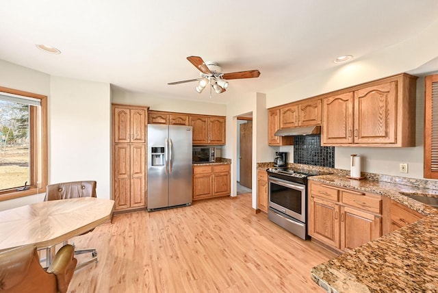 kitchen with light wood finished floors, under cabinet range hood, stone countertops, stainless steel appliances, and a ceiling fan