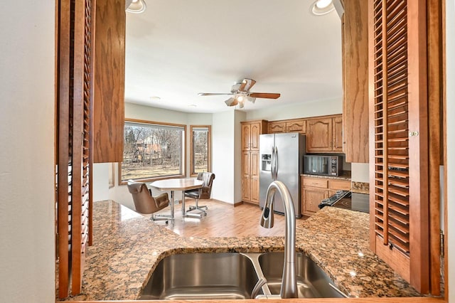 kitchen with a sink, black microwave, light stone counters, and stainless steel refrigerator with ice dispenser