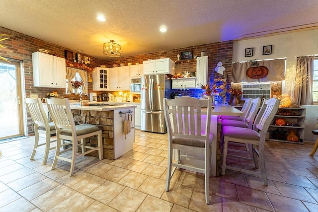 kitchen featuring white cabinets, brick wall, and freestanding refrigerator