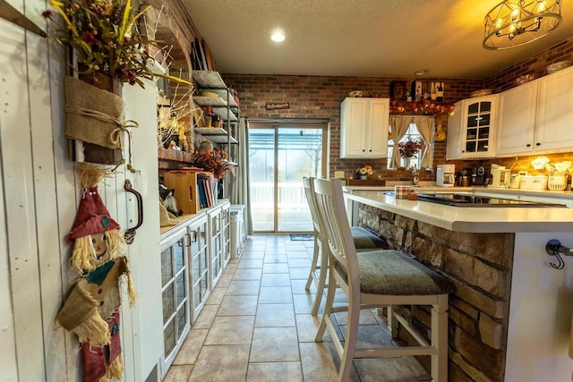 kitchen with glass insert cabinets, a textured ceiling, brick wall, and light countertops