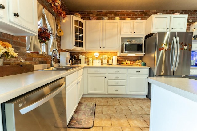 kitchen with appliances with stainless steel finishes, brick wall, light countertops, and a sink