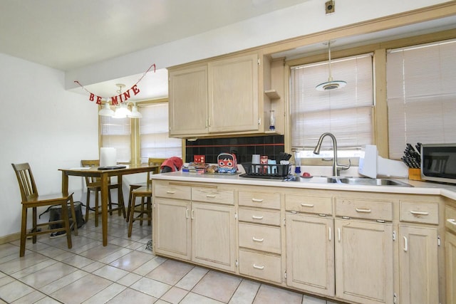 kitchen featuring a sink, light brown cabinetry, light countertops, stainless steel microwave, and backsplash