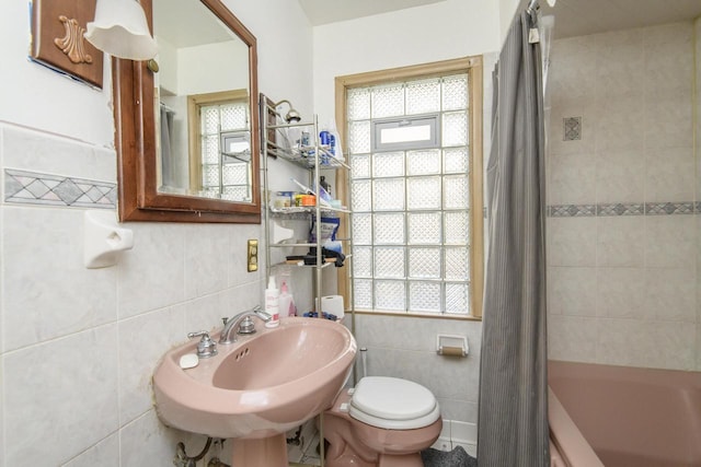 bathroom with tile walls, toilet, and a healthy amount of sunlight