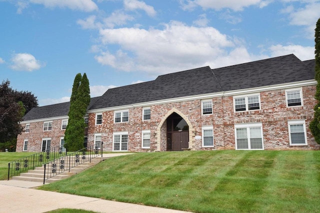 view of front of property featuring brick siding, roof with shingles, and a front lawn