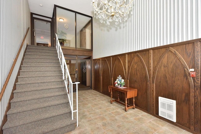 staircase featuring heating unit, wallpapered walls, wood walls, wainscoting, and a chandelier