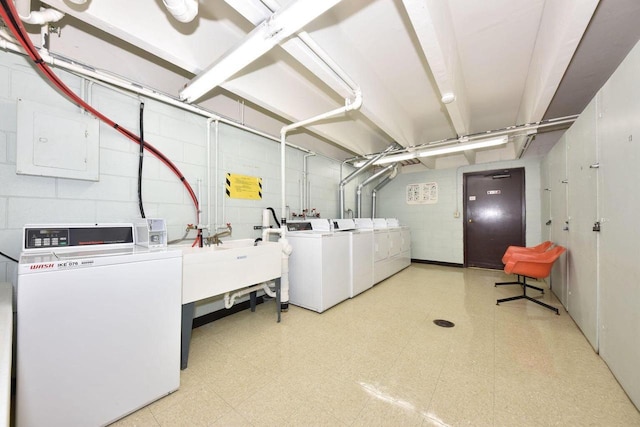 common laundry area featuring washing machine and clothes dryer, light floors, concrete block wall, and a sink