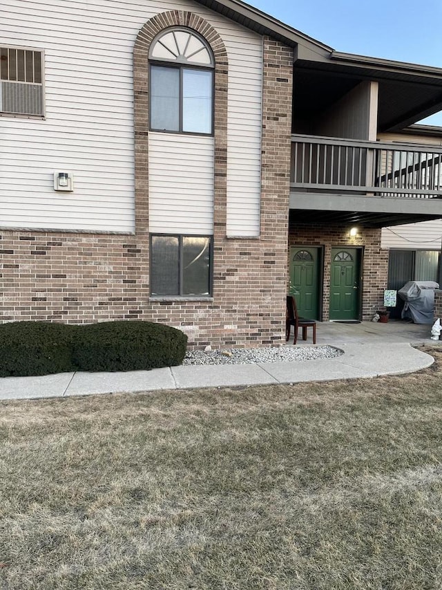 back of property with brick siding, a balcony, and a yard