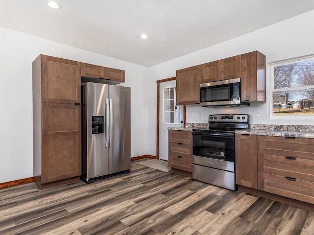 kitchen with baseboards, dark wood-style flooring, light stone countertops, and stainless steel appliances