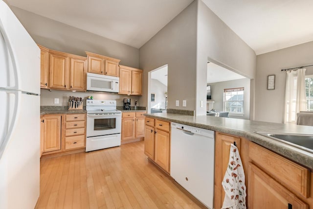 kitchen with white appliances, a sink, light brown cabinetry, light wood-style floors, and dark countertops