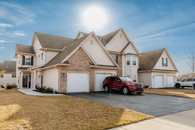 view of front facade with a front lawn, aphalt driveway, roof with shingles, a garage, and brick siding