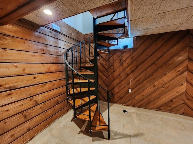 stairway featuring wooden walls and a drop ceiling