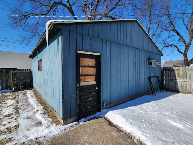 snow covered structure with a wall unit AC, an outdoor structure, and fence