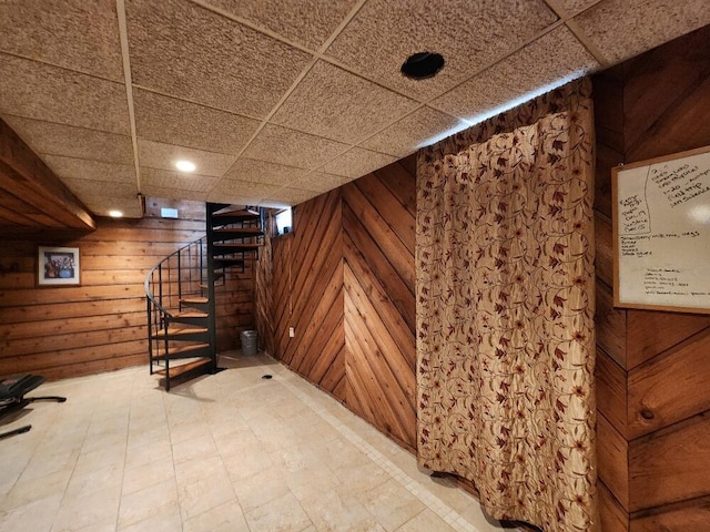 finished basement with stairway, a paneled ceiling, and wood walls