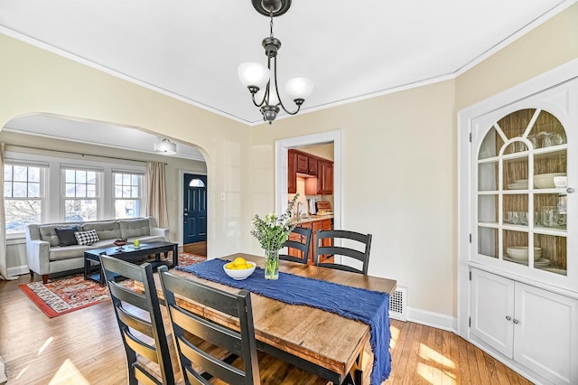 dining room with light wood-style flooring, arched walkways, an inviting chandelier, crown molding, and baseboards