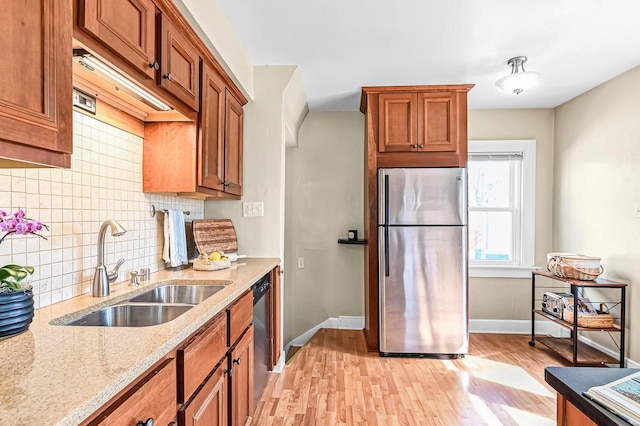 kitchen with light wood-type flooring, brown cabinets, a sink, light stone counters, and stainless steel appliances