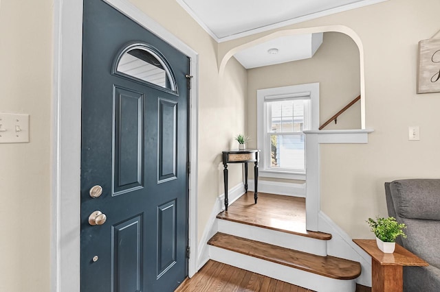 entrance foyer with arched walkways, ornamental molding, baseboards, and wood finished floors