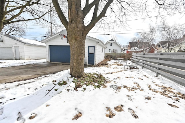 yard layered in snow with a garage, an outbuilding, and fence