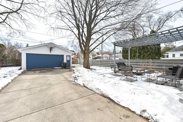 snow covered patio featuring a fire pit, a detached garage, fence, an outbuilding, and a pergola