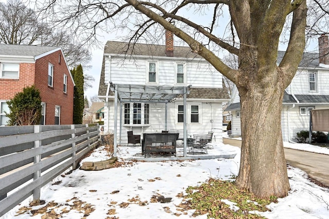 snow covered back of property with fence, roof with shingles, a pergola, a chimney, and a patio area