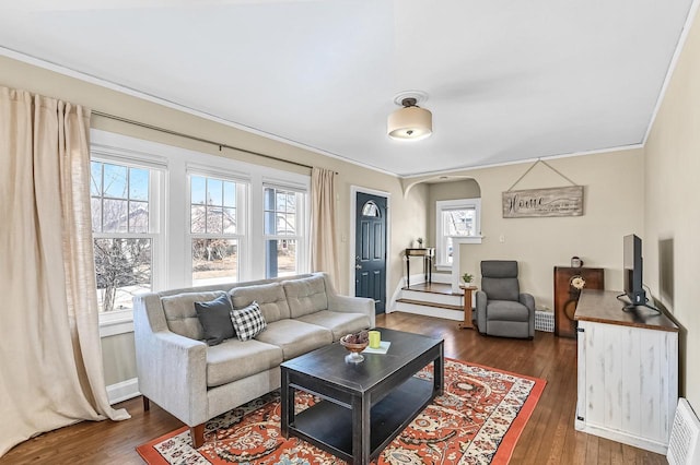 living room featuring arched walkways, dark wood-type flooring, and ornamental molding