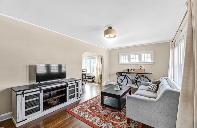 living area with baseboards, arched walkways, dark wood finished floors, and ornamental molding