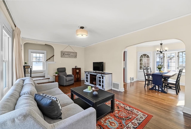 living area featuring visible vents, arched walkways, a notable chandelier, and wood finished floors