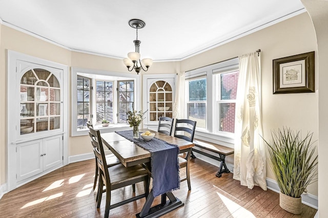 dining space featuring baseboards, wood-type flooring, an inviting chandelier, and ornamental molding