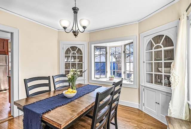 dining space with baseboards, light wood-type flooring, crown molding, and an inviting chandelier