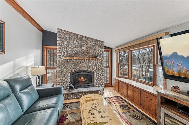 living area featuring a textured ceiling, a stone fireplace, light wood-style flooring, and vaulted ceiling