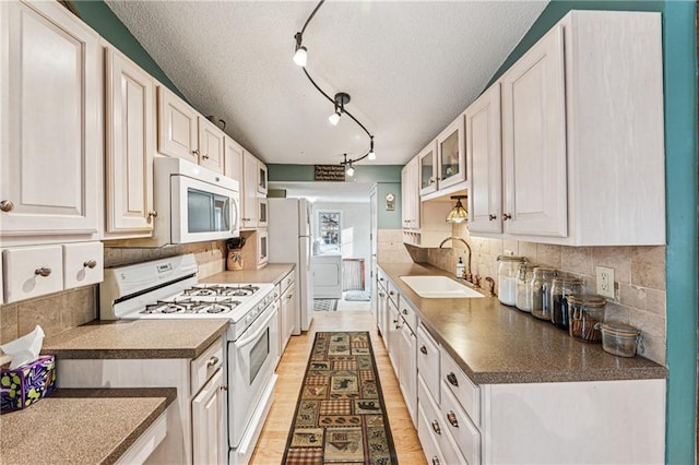 kitchen featuring white appliances, tasteful backsplash, light wood-type flooring, and a sink