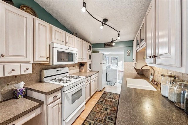 kitchen featuring a sink, white appliances, dark countertops, and washer / dryer