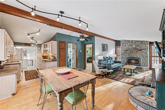 dining space featuring vaulted ceiling with beams, light wood finished floors, and a textured ceiling