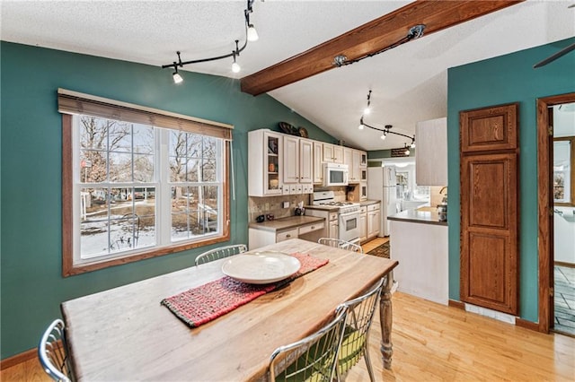 dining space with a textured ceiling, light wood-type flooring, lofted ceiling with beams, and baseboards