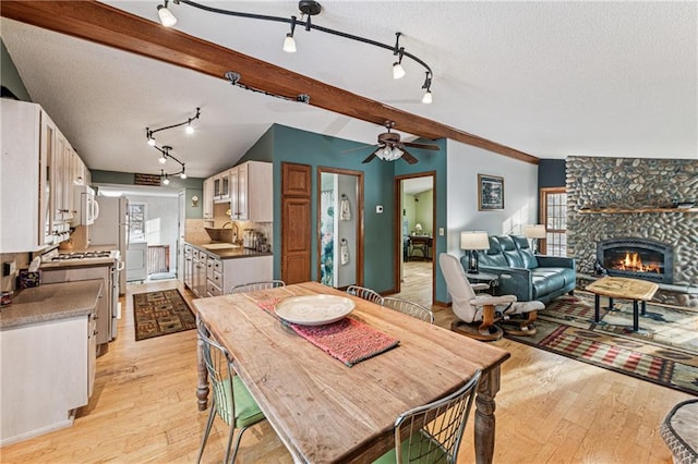 dining area with a stone fireplace, light wood-style flooring, a textured ceiling, and lofted ceiling with beams