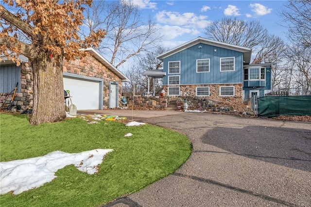 tri-level home with stone siding, driveway, an attached garage, and a front yard