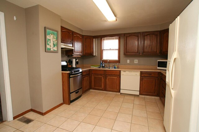 kitchen featuring white appliances, light countertops, under cabinet range hood, and a sink