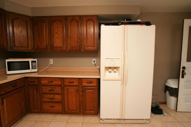 kitchen featuring light tile patterned floors, white appliances, brown cabinets, and light countertops