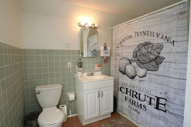 bathroom with a wainscoted wall, toilet, wood finished floors, tile walls, and vanity