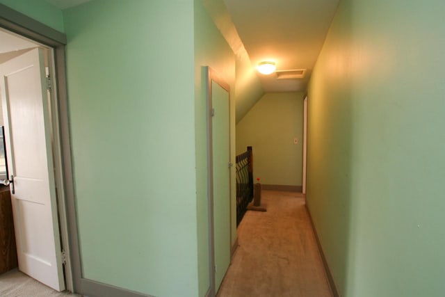 hall featuring baseboards, lofted ceiling, and light colored carpet