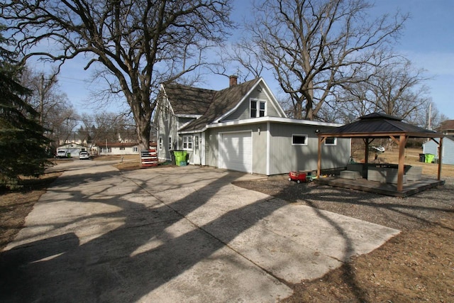 view of side of home with a gazebo, a garage, concrete driveway, and a chimney