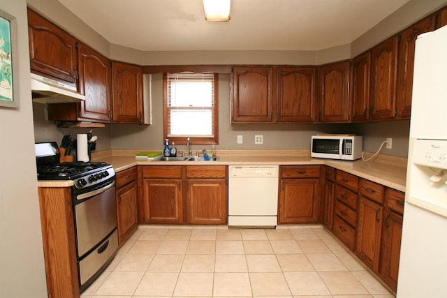 kitchen with under cabinet range hood, a sink, white appliances, brown cabinetry, and light countertops