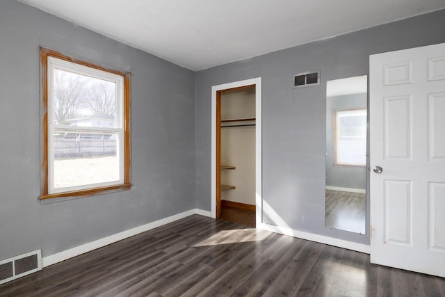 unfurnished bedroom with visible vents, multiple windows, and dark wood-type flooring