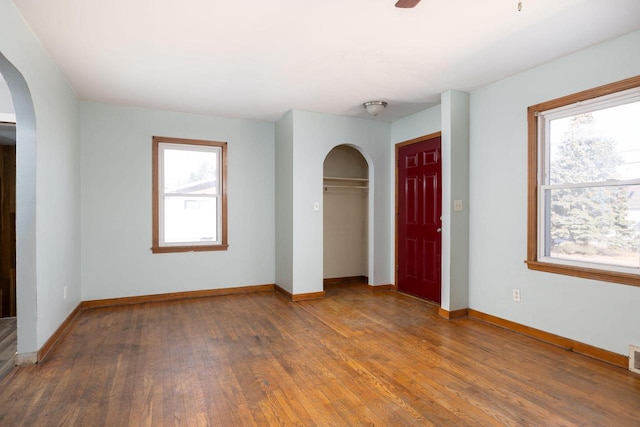 unfurnished bedroom featuring wood finished floors, arched walkways, a closet, and baseboards