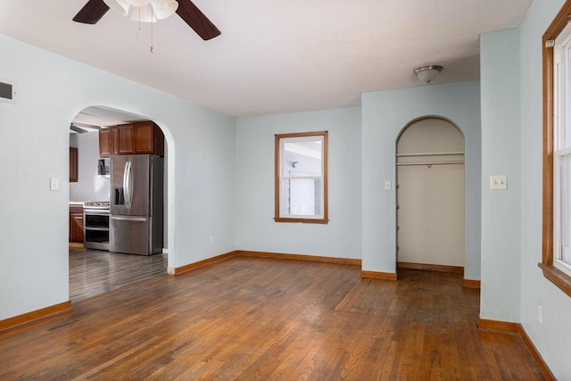 unfurnished living room with visible vents, arched walkways, dark wood-style flooring, and baseboards