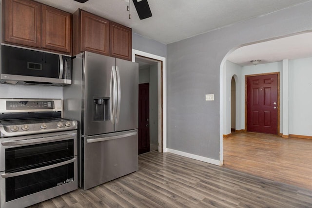 kitchen with a ceiling fan, wood finished floors, stainless steel appliances, arched walkways, and baseboards