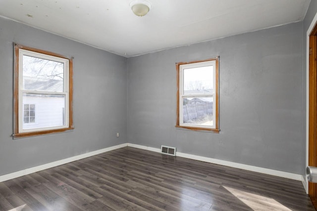 empty room with dark wood finished floors, baseboards, and visible vents