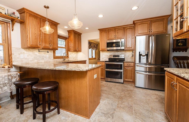 kitchen featuring light stone countertops, a peninsula, a sink, stainless steel appliances, and brown cabinets