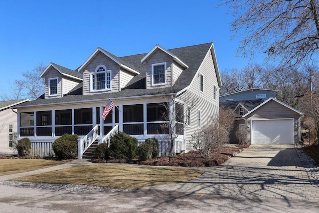 new england style home featuring an outbuilding, driveway, a sunroom, a shingled roof, and a garage